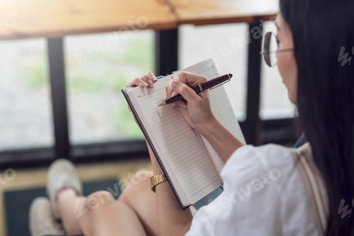 Preview: Close-up of a woman hand holding a pen with a notebook taking note concept.