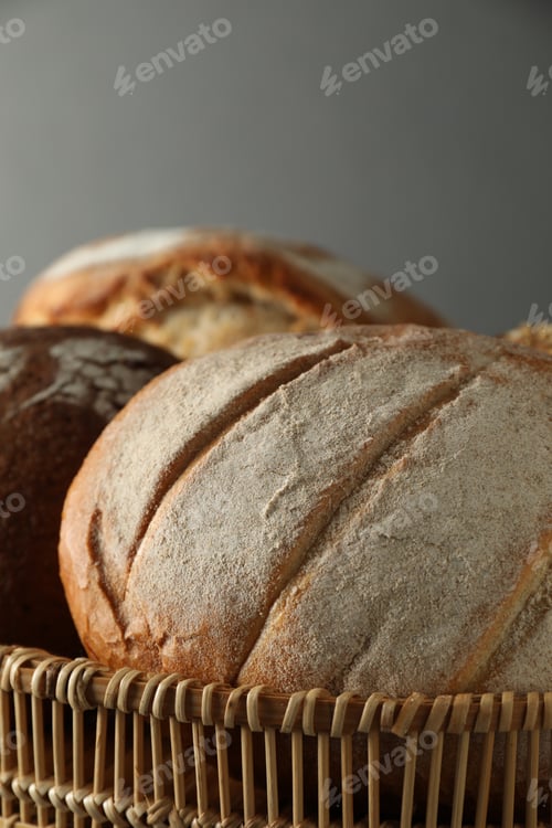 Preview: Wicker basket with different types of fresh bread against grey background, closeup