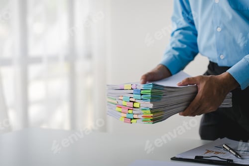 Preview: Businessman working on stacks of documents to search for information and check documents on office d