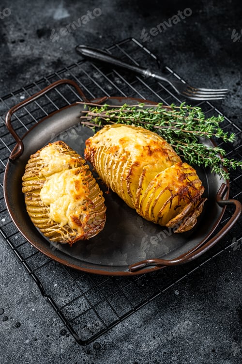 Preview: Baked hasselback potatoes with cheese, garlic, thyme and rosemary. Black background. Top view