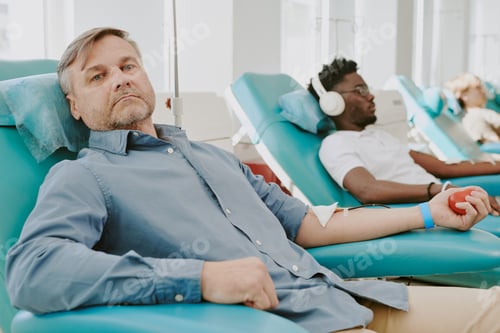Preview: Middle Aged Caucasian Man Donating Blood Beside Young Black Man Relaxing