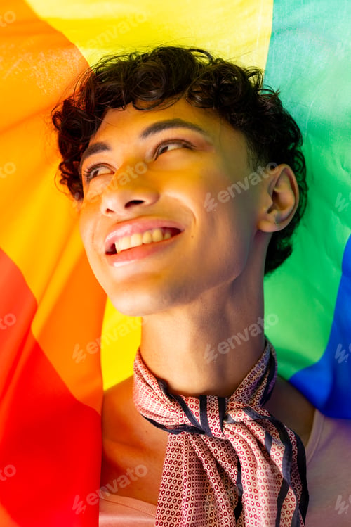 Preview: Smiling young man wrapped in rainbow flag, celebrating LGBTQ+ pride and identity