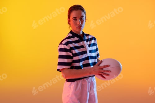 Preview: Portrait of caucasian female rugby player with rugby ball over neon yellow lighting