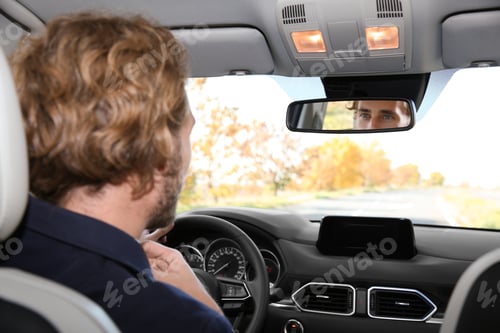 Preview: Young handsome man looking into interior mirror in car