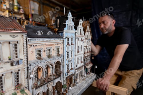 Preview: Model maker man working at scale model of miniature building in his workshop full of tools