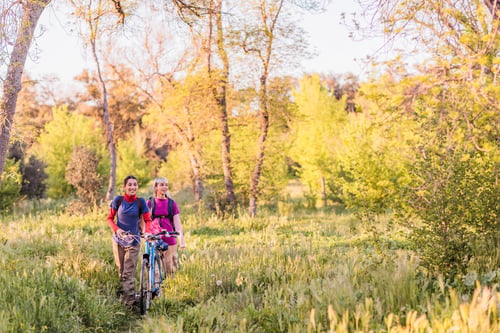 Preview: Two female friends walking with bicycle in nature during golden hour