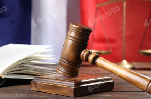 Preview: Judge's gavel, book and scales on wooden table against flag of France, closeup