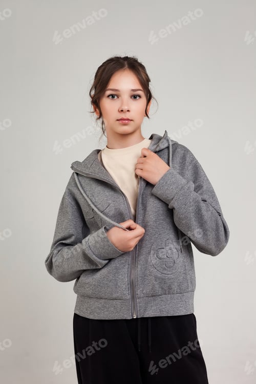 Preview: Casual Teen Girl Standing Indoors in a Gray Hoodie With Hands Near Zipper