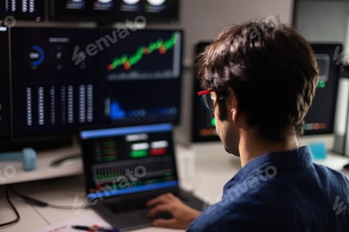 Preview: Back view of man in blue shirt working with multiple screens and laptop. Stock market and trading.