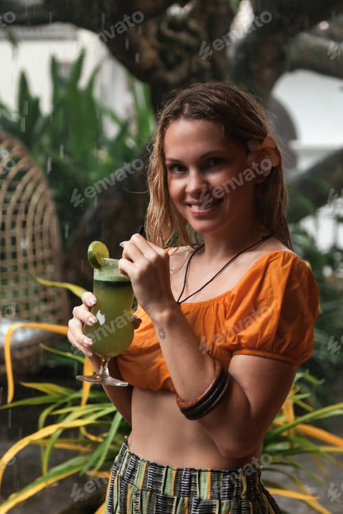 Preview: Happy young woman with fresh cocktail in the tropical rain