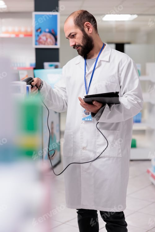 Preview: Pharmacist in white coat holding tablet computer typing vitamins barcode while doing drugs inventory