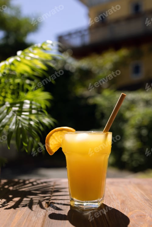 Preview: Glass of fresh orange juice on a wooden table under a palm tree branch