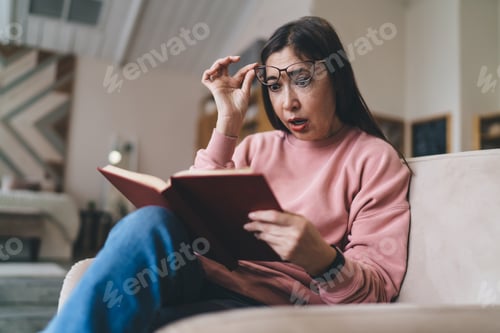 Preview: Surprised elderly Asian lady reading book in living room