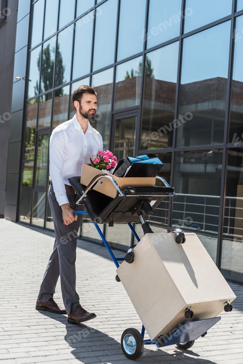 Vorschau: entlassener junger Manager mit Kisten auf einem Rollwagen