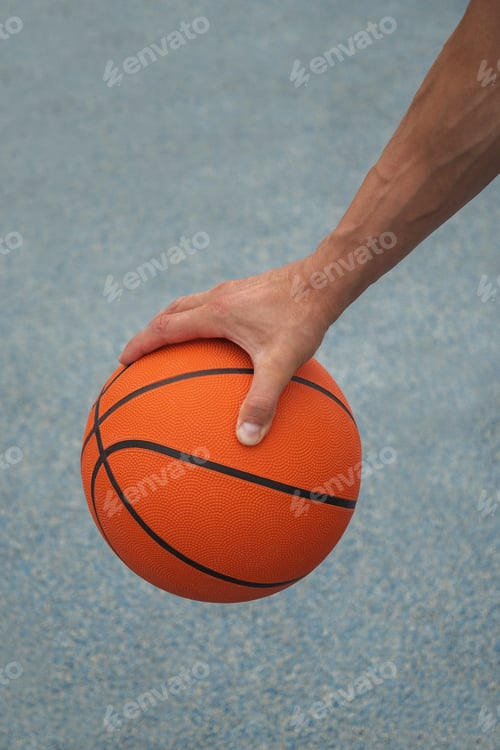 Preview: Basketball orange ball in man hand on blue court. Sport background.