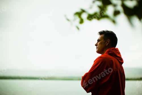 Vista previa: A middle aged man in a red jacket looking over water, deep in thought.