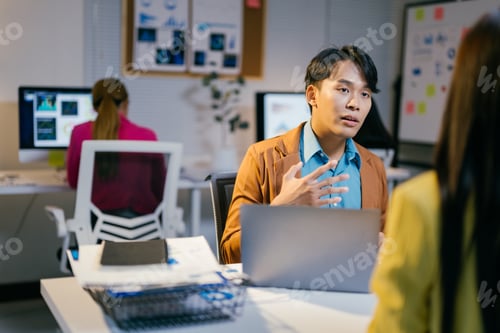 Preview: Energetic asian manager gestures while discussing work with an employee in a modern office at night,