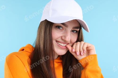Preview: Portrait of smiling woman in stylish baseball hat on light blue background, closeup