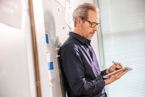 Preview: Male digital designer leaning against office wall making notes