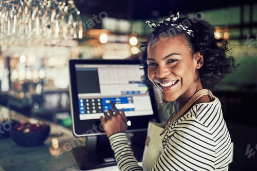 Preview: Smiling African waitress using a restaurant point of sale terminal
