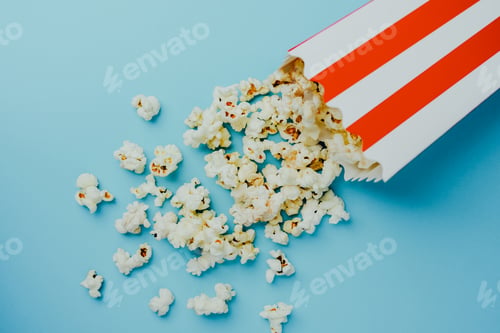Preview: Popcorn spilling out of striped container on a blue surface