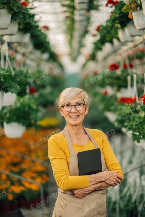 Preview: Portrait of happy old florist with tablet at hothouse smiling at camera