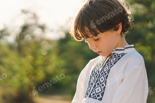 Preview: A young child wearing a traditional embroidered shirt quietly prays outdoors
