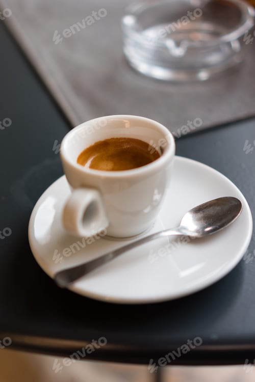 Preview: Vertical shot of a cup of delicious espresso with a spoon on a black table