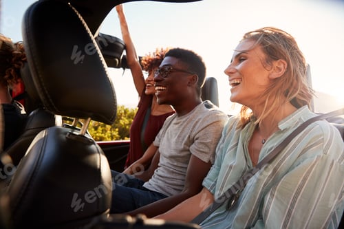 Preview: Happy young adult friends on a road trip vacation travelling in the back of an open car