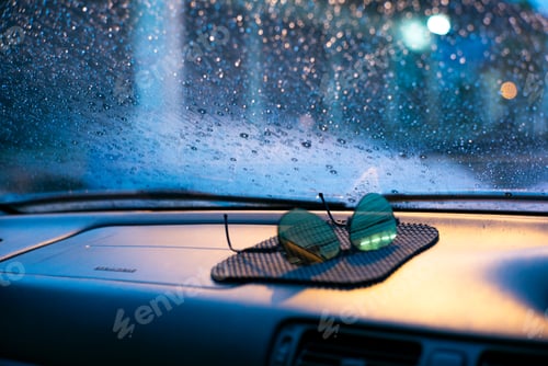 Preview: Defused sunglasses on the car console with front glass of the car and rain drop in background