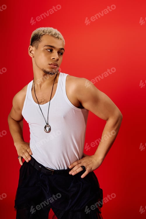 Preview: Young man showcases trendy style in red studio setting with confidence and flair