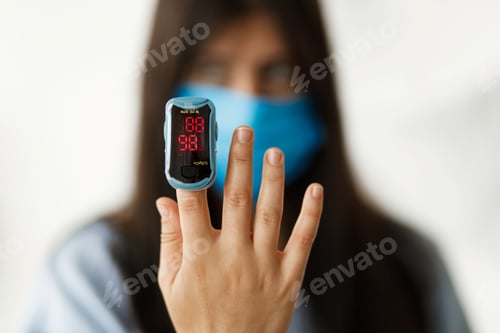 Preview: Pulse Oximeter on finger, adult female in face mask measuring blood oxygen level