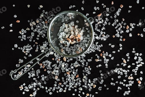 Preview: Himalayan pink salt and a strainer on black background, top view photo