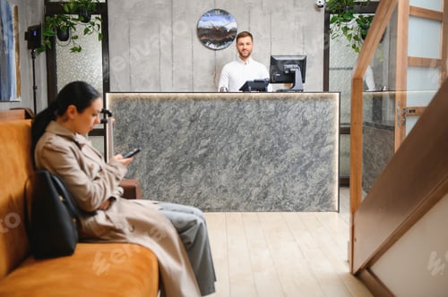 Preview: Businesswoman with luggage in modern hotel lobby using smartphone