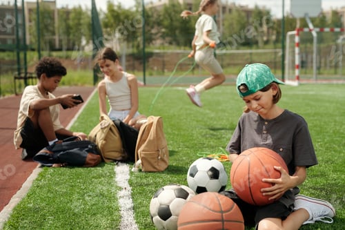 Preview: Cute schoolboy looking at basketball ball in his hands while choosing item