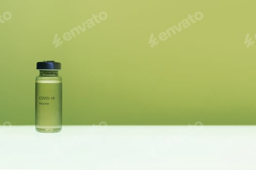 Preview: Selective focus shot of a COVID-19 vaccine in a bottle isolated on a green and white background