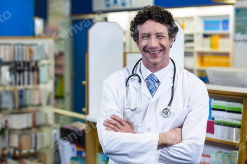 Preview: Male doctor standing in pharmacy wearing stethoscope by shelves with medicine boxes and smiling