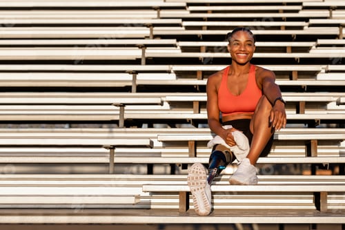 Preview: Woman athlete with prosthetic leg smiling carrying a towel and sitting to rest