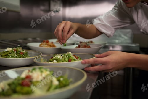 Preview: Female chef garnishing appetizer plates at order station