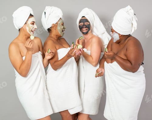 Preview: Delighted multiethnic women with cucumbers during spa session