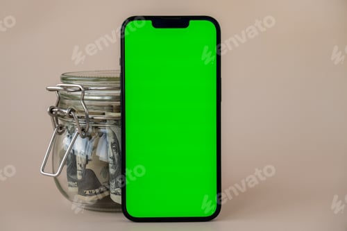Preview: Vertical Green screen on modern mobile phone in background of glass jar full of American currency
