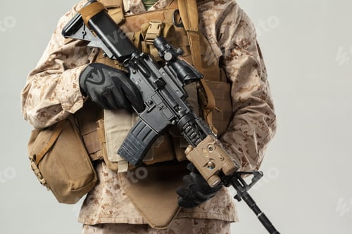 Preview: Military personnel holds an assault rifle with tactical gear in a neutral space