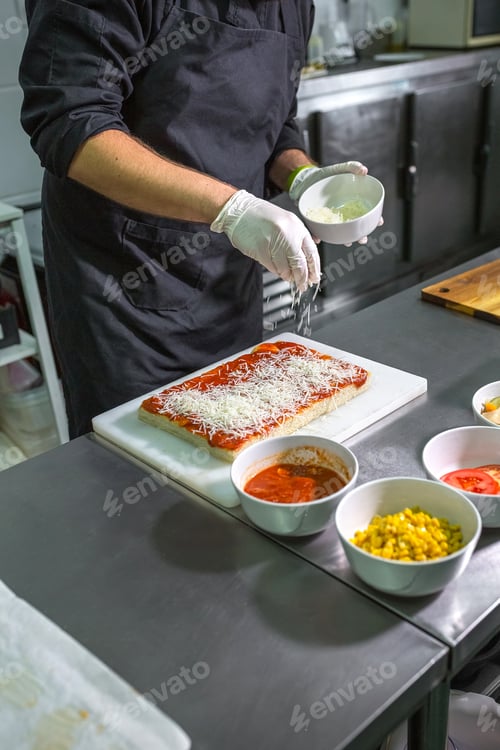 Preview: Unrecognizable male chef sprinkling grated cheese over tomato sauced focaccia in restaurant kitchen