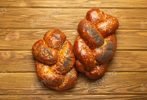 Preview: Two reshly baked Challah bread covered with poppy and sesame seeds, top view on rustic wooden