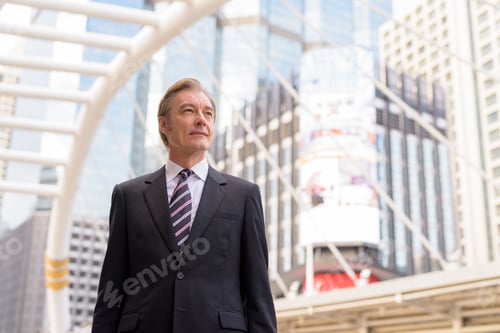 Preview: Mature handsome businessman in suit thinking at skywalk bridge in the city
