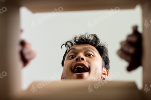 Preview: Happy Asian Male Peering Into Box Joyfully Reacting To Contents From Below