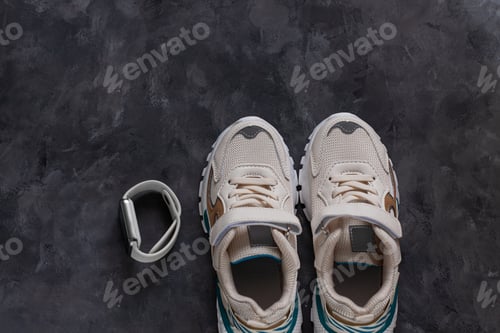 Preview: White kids sneakers on a dark grey background flat lay in minimal style. Trendy sports shoes, active