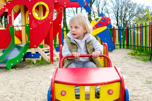 Preview: Cute blond little young toddler kid child boy sitting and riding in toy car,bus, train in playground