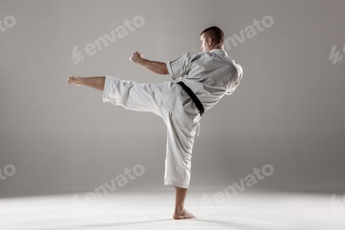 Preview: Man In White Kimono And Black Belt Training Karate Over Gray Background.