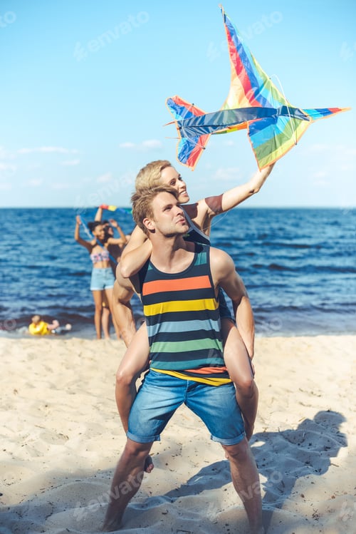 Preview: selective focus of couple with colorful kite with multiracial friends behind spending time on sandy